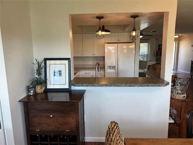 kitchen featuring pendant lighting, white cabinetry, dark stone countertops, white refrigerator with ice dispenser, and kitchen peninsula