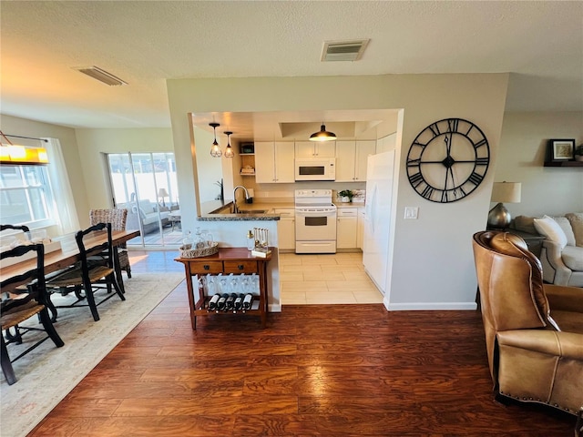 kitchen with white cabinetry, wood-type flooring, white appliances, kitchen peninsula, and a textured ceiling