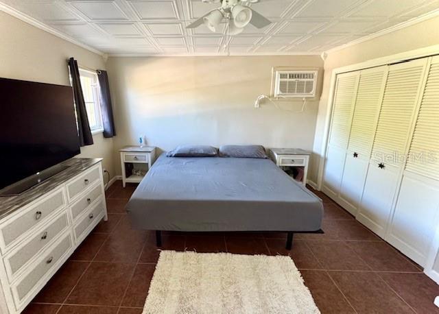 tiled bedroom with a wall unit AC, ceiling fan, and a closet