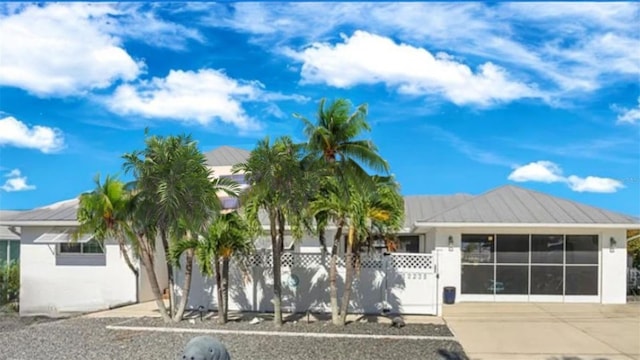 view of front of property featuring a standing seam roof, driveway, a fenced front yard, metal roof, and stucco siding