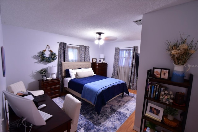 bedroom featuring visible vents, multiple windows, a textured ceiling, and wood finished floors