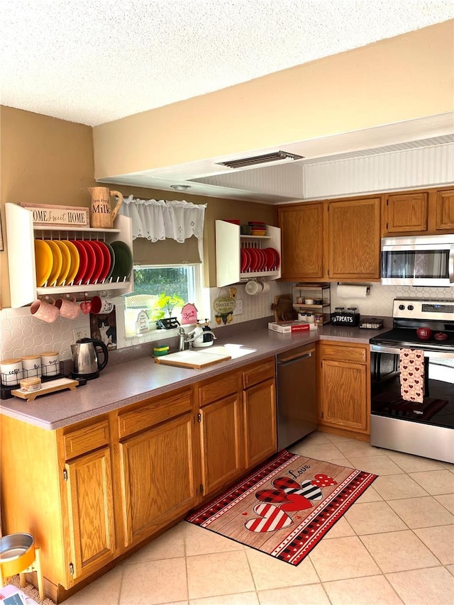 kitchen with a sink, tasteful backsplash, appliances with stainless steel finishes, brown cabinetry, and light tile patterned floors