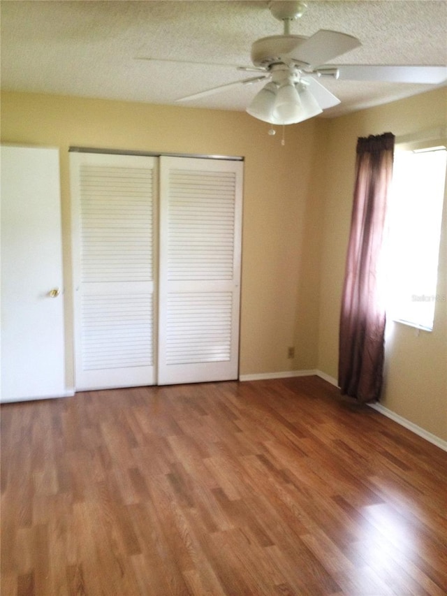 unfurnished bedroom featuring baseboards, wood finished floors, a closet, and a textured ceiling