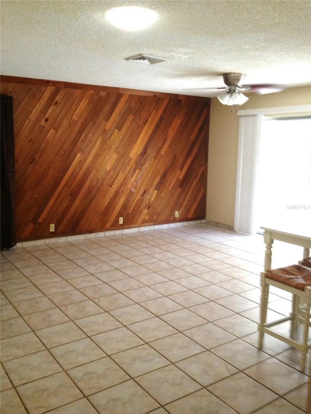 empty room featuring visible vents, a textured ceiling, wooden walls, light tile patterned floors, and ceiling fan