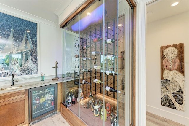 wine area with light hardwood / wood-style floors, wet bar, crown molding, and beverage cooler