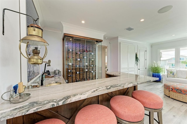 bar featuring light hardwood / wood-style floors, sink, light stone countertops, and crown molding