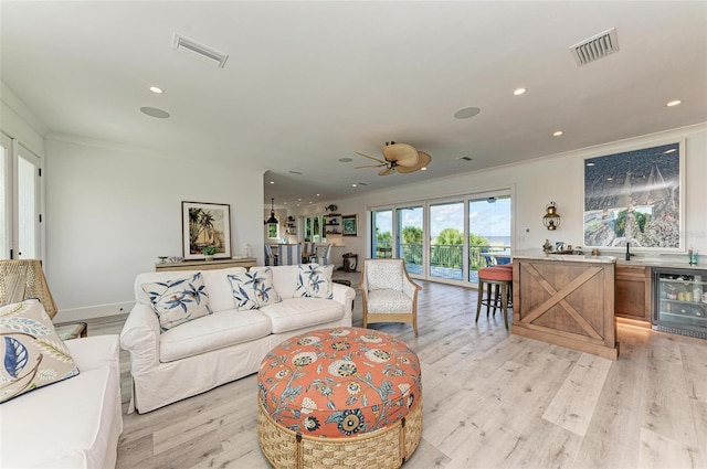 living room featuring ceiling fan, light wood-type flooring, crown molding, and beverage cooler