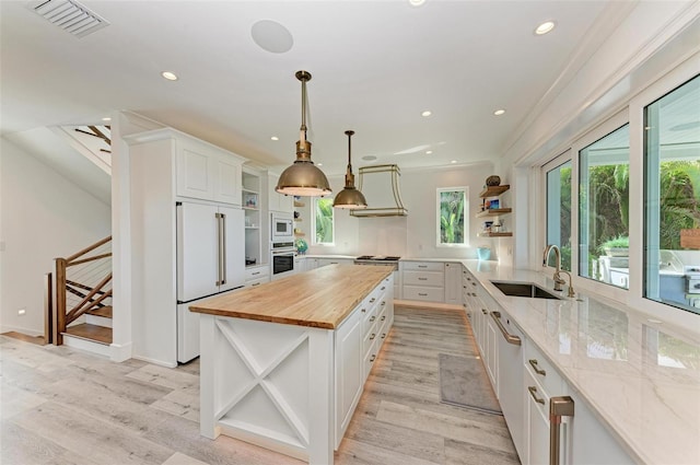 kitchen with sink, built in appliances, white cabinets, a center island, and butcher block countertops