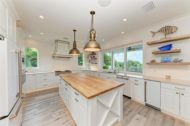 kitchen featuring stainless steel appliances, decorative light fixtures, white cabinets, butcher block countertops, and a kitchen island