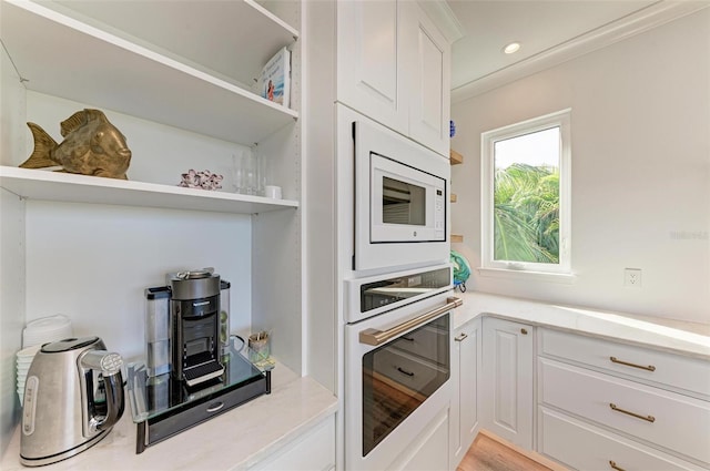 kitchen featuring white appliances, light hardwood / wood-style floors, white cabinetry, and ornamental molding