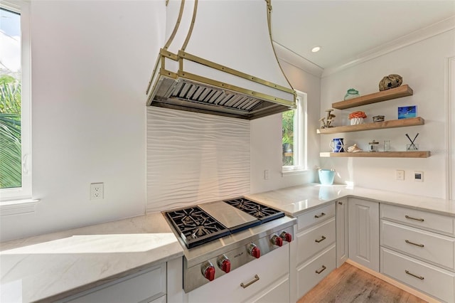 kitchen featuring stainless steel gas stovetop, ventilation hood, light hardwood / wood-style flooring, ornamental molding, and light stone counters