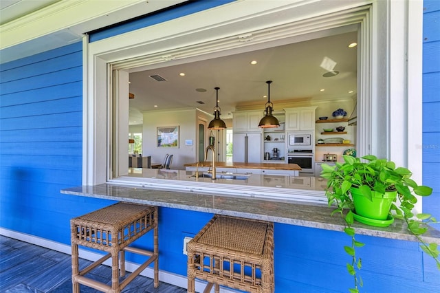 bar featuring sink, oven, decorative light fixtures, white microwave, and ornamental molding