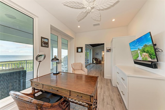 home office with light wood-type flooring, a water view, and ceiling fan