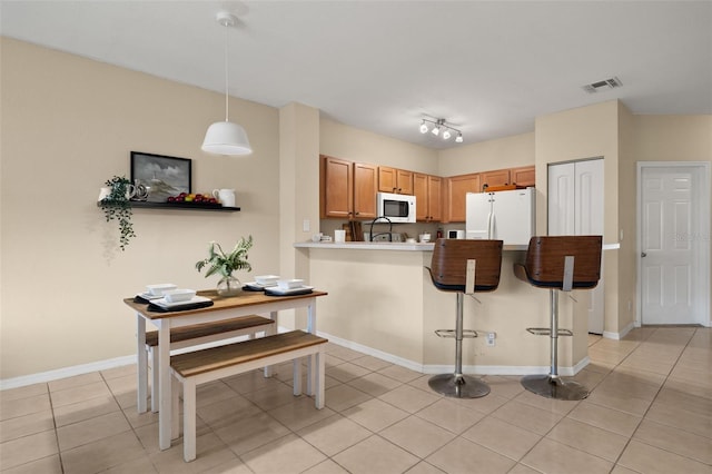 kitchen with kitchen peninsula, light tile patterned flooring, white appliances, hanging light fixtures, and a breakfast bar area