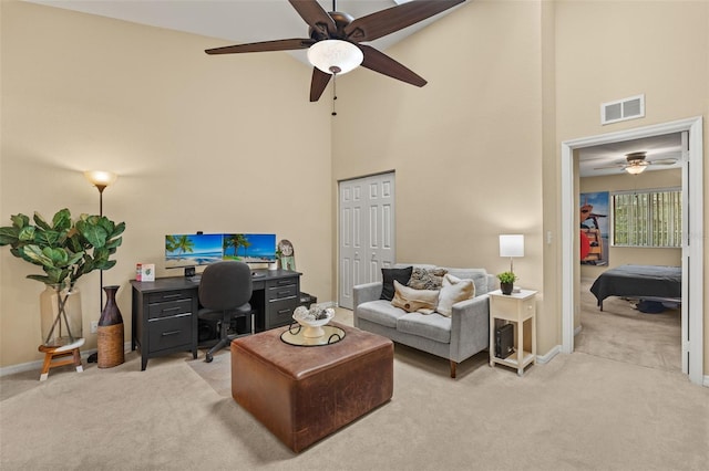 carpeted home office featuring ceiling fan and a high ceiling