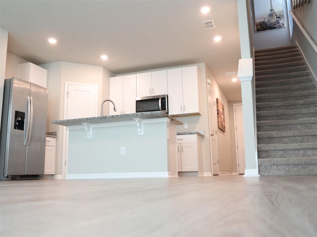 kitchen featuring white cabinets, a kitchen breakfast bar, stainless steel appliances, and light stone counters