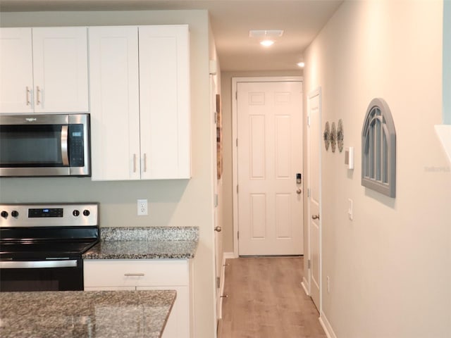 kitchen featuring white cabinets, light hardwood / wood-style floors, dark stone countertops, and stainless steel appliances