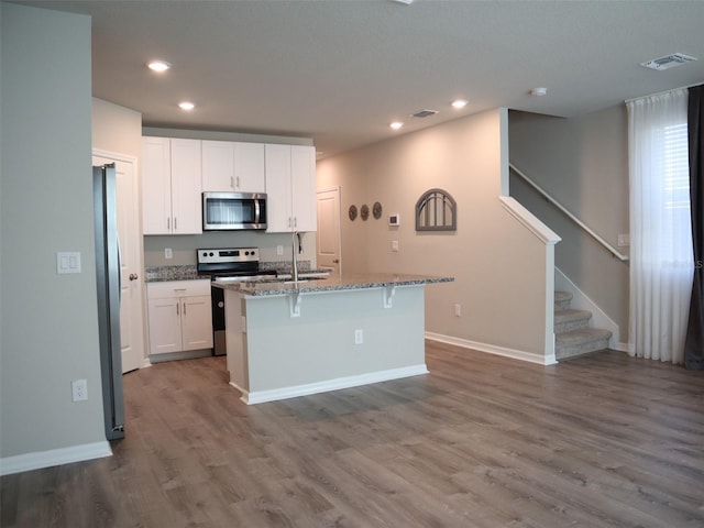 kitchen with a kitchen bar, appliances with stainless steel finishes, a kitchen island with sink, hardwood / wood-style floors, and white cabinetry