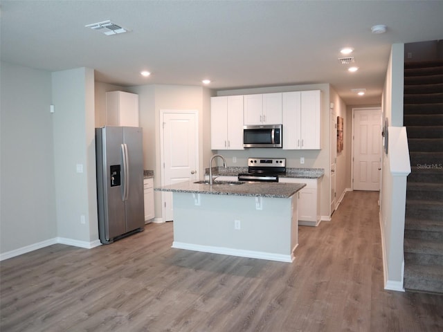 kitchen with stainless steel appliances, sink, light hardwood / wood-style flooring, white cabinets, and an island with sink