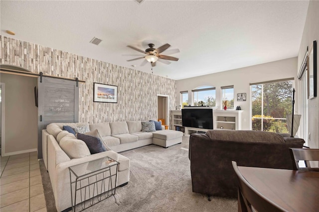 living room with ceiling fan, a barn door, light tile patterned floors, and a textured ceiling