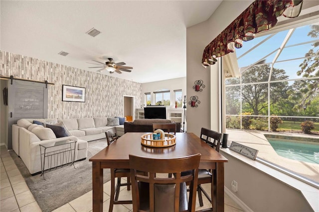 dining room featuring ceiling fan, a barn door, and light tile patterned flooring