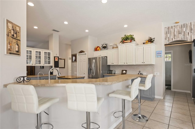 kitchen with stainless steel fridge, light tile patterned floors, white cabinetry, and a kitchen breakfast bar