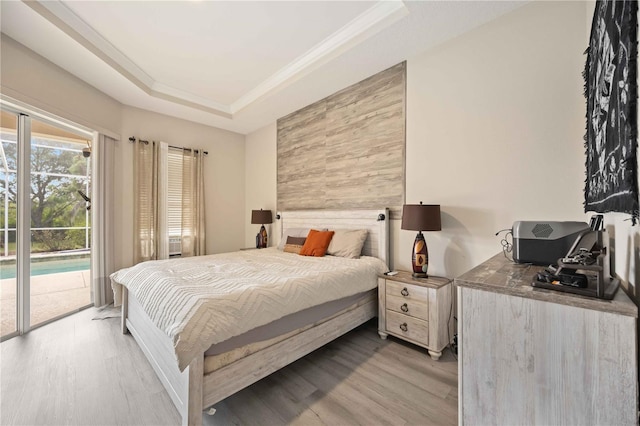 bedroom featuring a raised ceiling, light wood-type flooring, ornamental molding, and access to outside