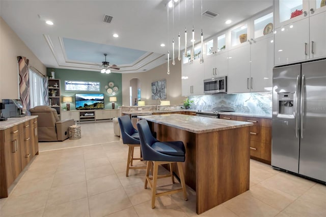 kitchen with appliances with stainless steel finishes, a center island, white cabinets, a breakfast bar area, and a raised ceiling