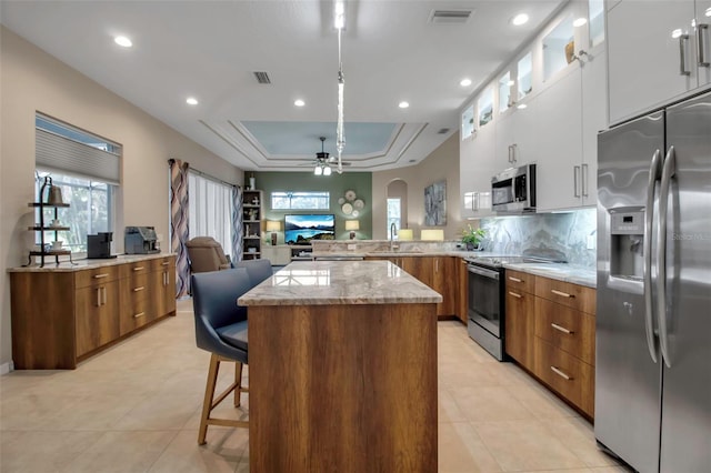 kitchen featuring a kitchen bar, appliances with stainless steel finishes, kitchen peninsula, white cabinets, and a raised ceiling