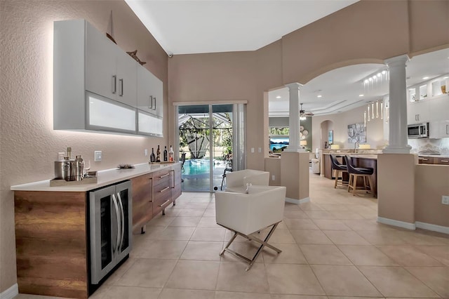 kitchen featuring white cabinetry, wine cooler, ornate columns, ceiling fan, and a kitchen bar