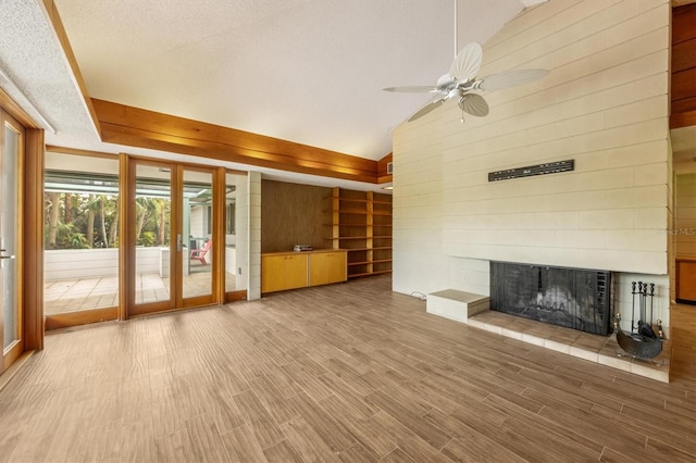 unfurnished living room with ceiling fan, french doors, vaulted ceiling, a tiled fireplace, and wooden walls