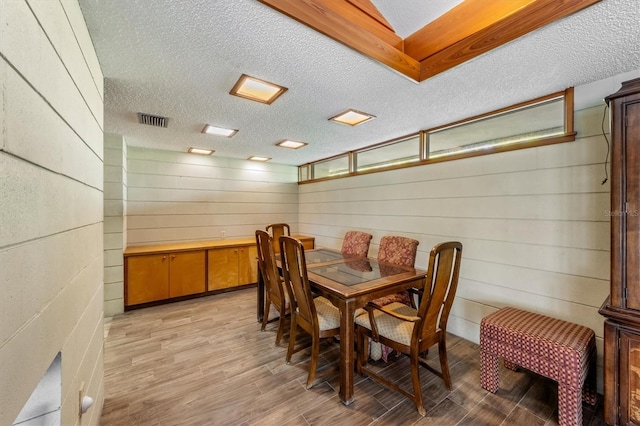 dining area featuring wooden walls, light hardwood / wood-style flooring, and a textured ceiling