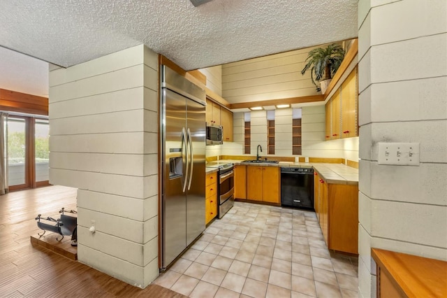 kitchen featuring a textured ceiling, sink, stainless steel appliances, and wood walls