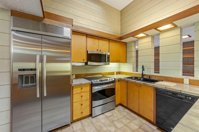 kitchen featuring appliances with stainless steel finishes, tile counters, wooden walls, and sink