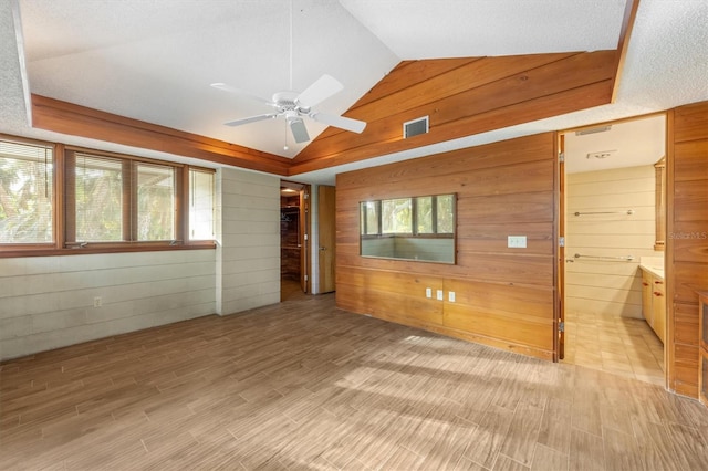 unfurnished room with vaulted ceiling, ceiling fan, a healthy amount of sunlight, and wood walls