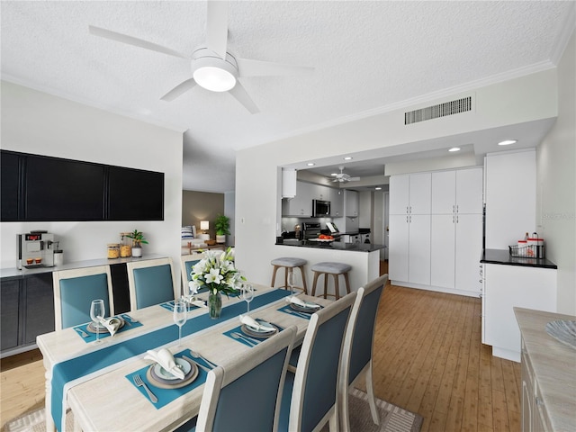 dining area with light wood-type flooring, a textured ceiling, ceiling fan, and crown molding