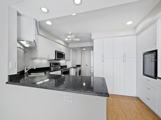 kitchen with dark stone counters, kitchen peninsula, sink, appliances with stainless steel finishes, and white cabinetry