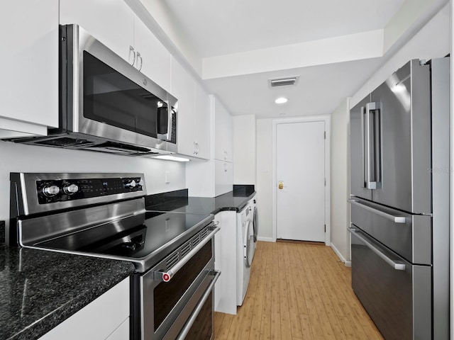 kitchen with stainless steel appliances, light hardwood / wood-style flooring, washer / clothes dryer, dark stone counters, and white cabinets