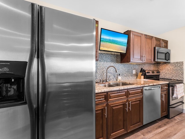 kitchen with light stone countertops, tasteful backsplash, stainless steel appliances, sink, and light hardwood / wood-style floors