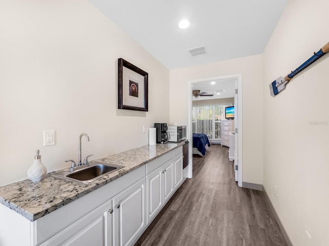 interior space featuring sink, ceiling fan, white cabinetry, light stone counters, and wood-type flooring