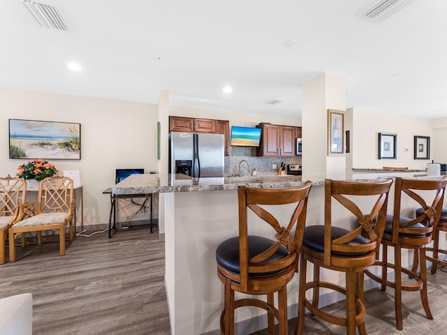 kitchen featuring a kitchen breakfast bar, tasteful backsplash, light stone counters, dark hardwood / wood-style floors, and appliances with stainless steel finishes