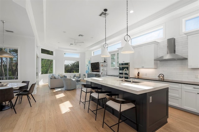 kitchen featuring white cabinets, a kitchen breakfast bar, wall chimney range hood, and decorative light fixtures