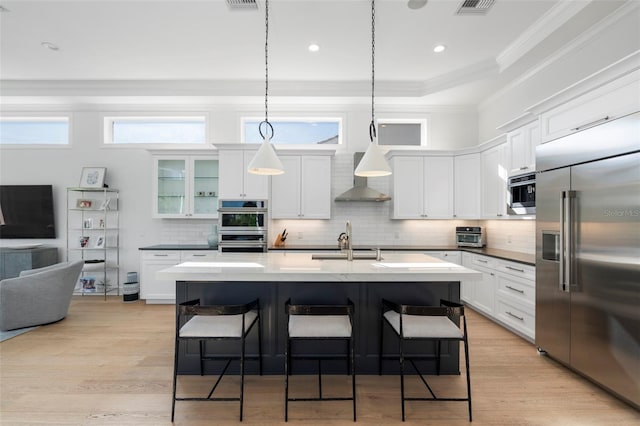 kitchen with white cabinets, wall chimney exhaust hood, pendant lighting, and appliances with stainless steel finishes