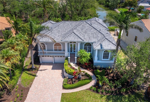 view of front facade featuring a water view, stucco siding, decorative driveway, a tile roof, and a garage