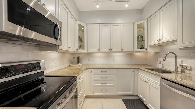 kitchen with stainless steel appliances, white cabinetry, light stone counters, and sink