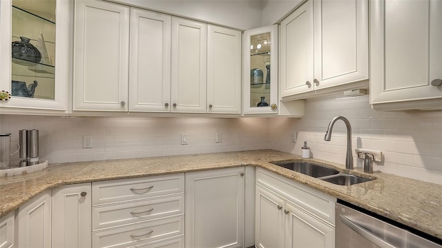 kitchen with backsplash, dishwasher, sink, white cabinetry, and light stone countertops