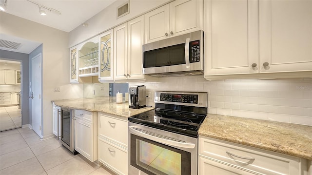 kitchen with white cabinets, stainless steel appliances, backsplash, light stone counters, and light tile patterned floors