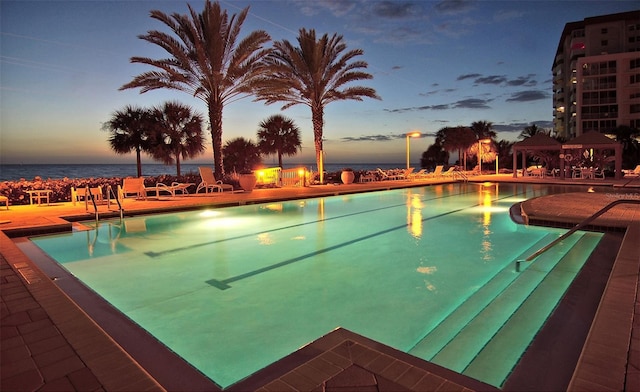 pool at dusk featuring a water view and a patio