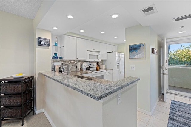 kitchen with white appliances, sink, kitchen peninsula, light stone countertops, and white cabinetry