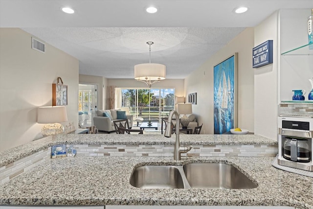 kitchen with pendant lighting, plenty of natural light, light stone counters, and sink